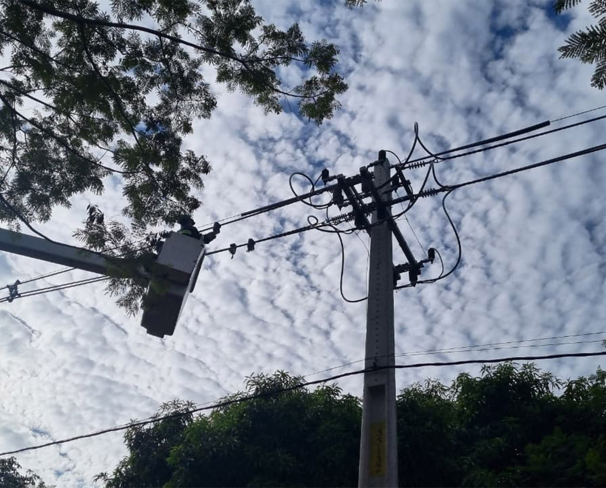 Operario en la canasta de un hidroelevador trabajando sobre una línea aérea de media tensión, vista desde abajo contra el cielo