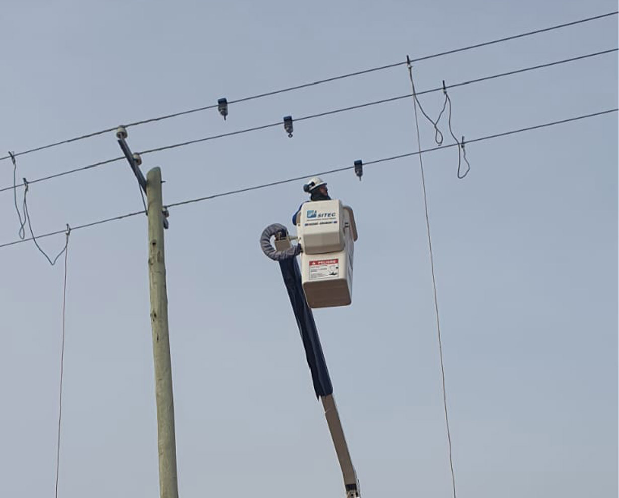 Operario con casco en la canasta de un hidroelevador montando detectores sobre los conductores de una línea aérea