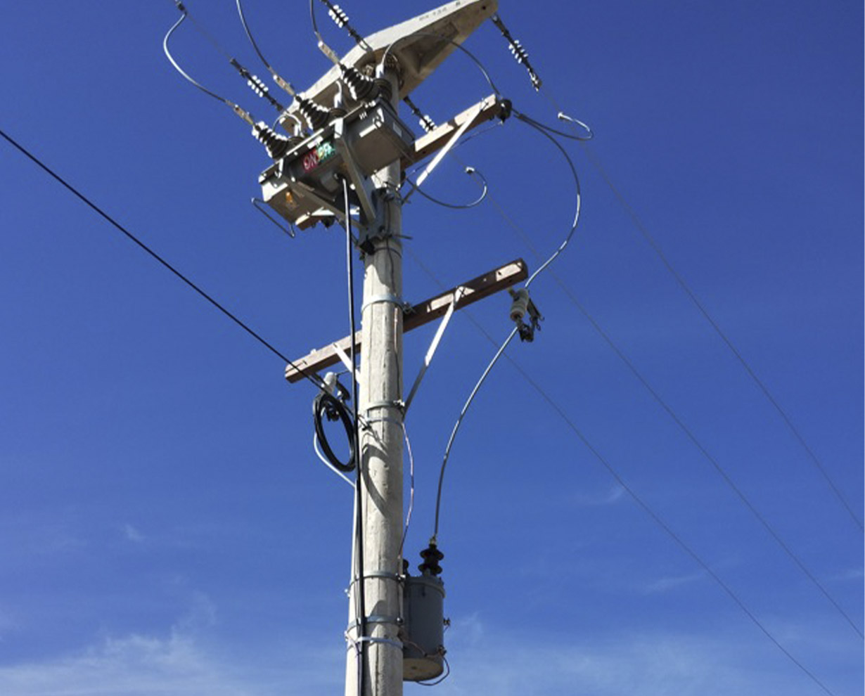 Reconectador montado en la cima de un poste de hormigón, con sus aisladores y cables de maniobra contra el cielo